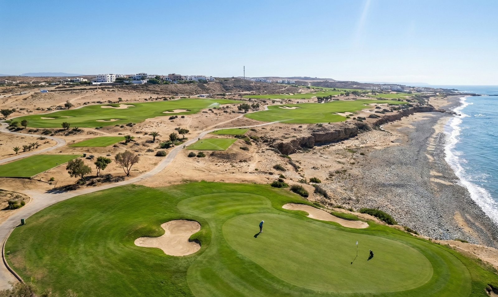 Deux joueurs sur le green du trou 14, le parcours en service, la côte rocheuse et l'océan sur la droite.